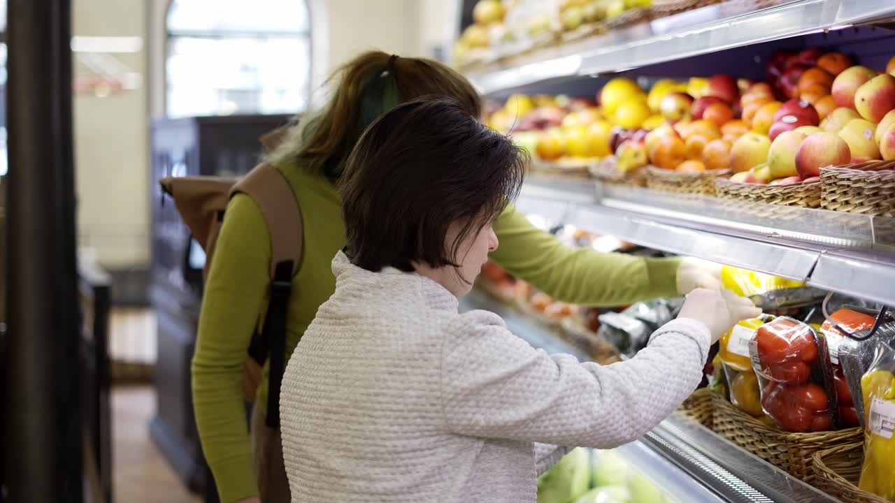 chica con síndrome de down con su madre tomando verduras del estante en el supermercado