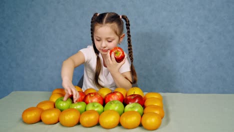 little girl eating juicy apple. fresh organic fruit nicely placed on the table. happy small girl with ripe fruits on blue background.