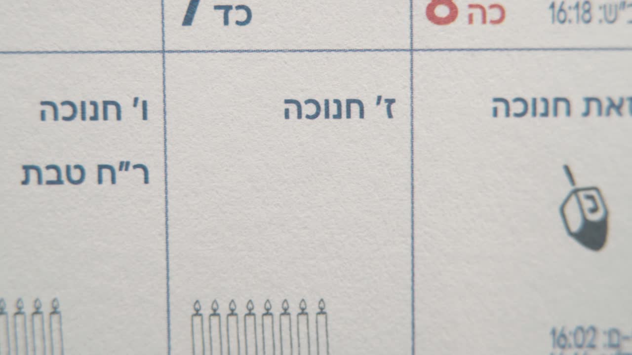 un macro pan a la izquierda plano suave y lento de un calendario judío, fechas israelíes, fiesta de hanukkah, dibujos de velas, mes y horario semanal, video 4k
