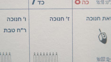un macro pan a la izquierda plano suave y lento de un calendario judío, fechas israelíes, fiesta de hanukkah, dibujos de velas, mes y horario semanal, video 4k