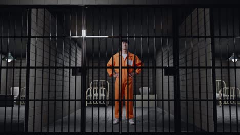 full body of asian male prisoner in broken handcuffs standing with arms akimbo in prison, raising head and looking to camera