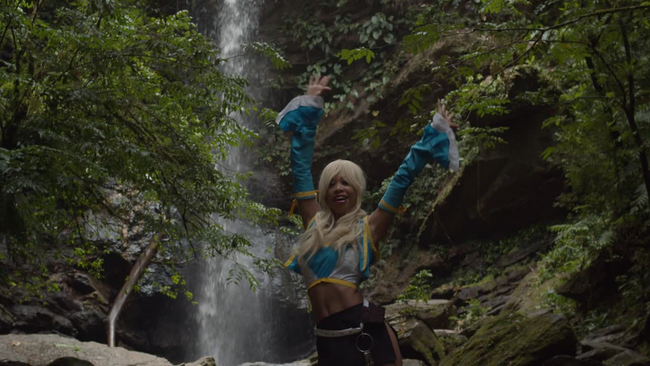 chica fitness increíble en un disfraz de anime cosplayer disfrutando de la naturaleza en la base de una cascada épica