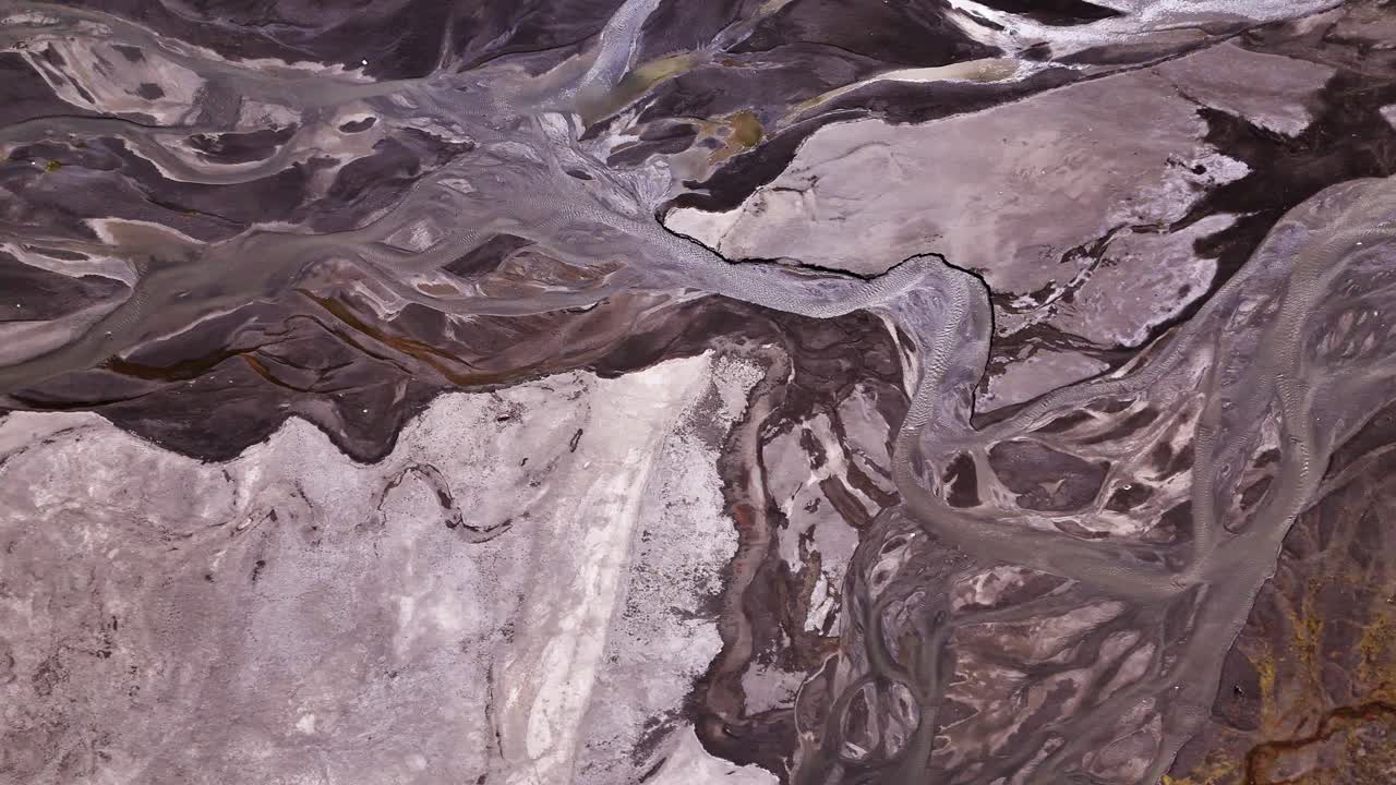 Melting icy water creating abstract curvy stream as it meanders over glacial flat stony lands to mountain lake. Drone Birds Eye view