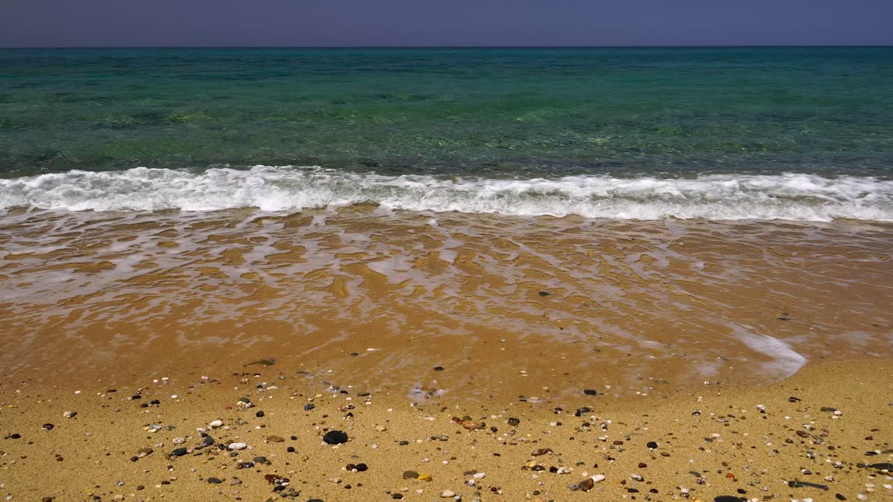 잔잔한 파도가 작고 매끄러운 흩어진 돌들로 황금빛 해변을 씻는다