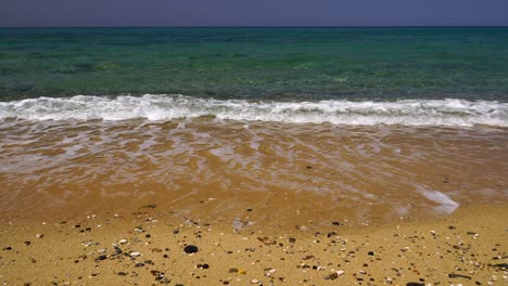 Suaves-Olas-Se-Lavan-En-Una-Playa-Dorada-Con-Pequeñas-Piedras-Lisas-Dispersas