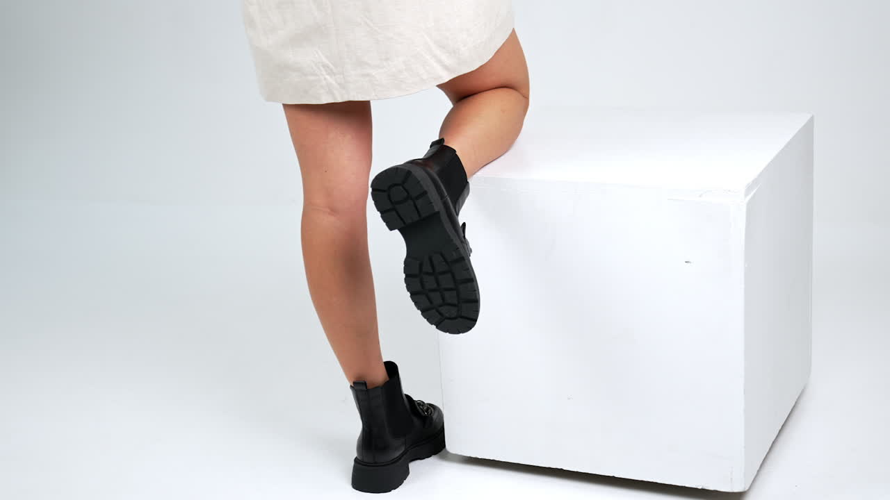 Woman in Black Ankle Boots and Beige Dress on White Background