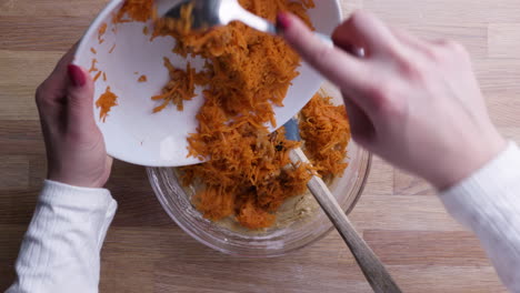 manos agregando zanahorias ralladas con una cucharada en masa de pastel de zanahoria