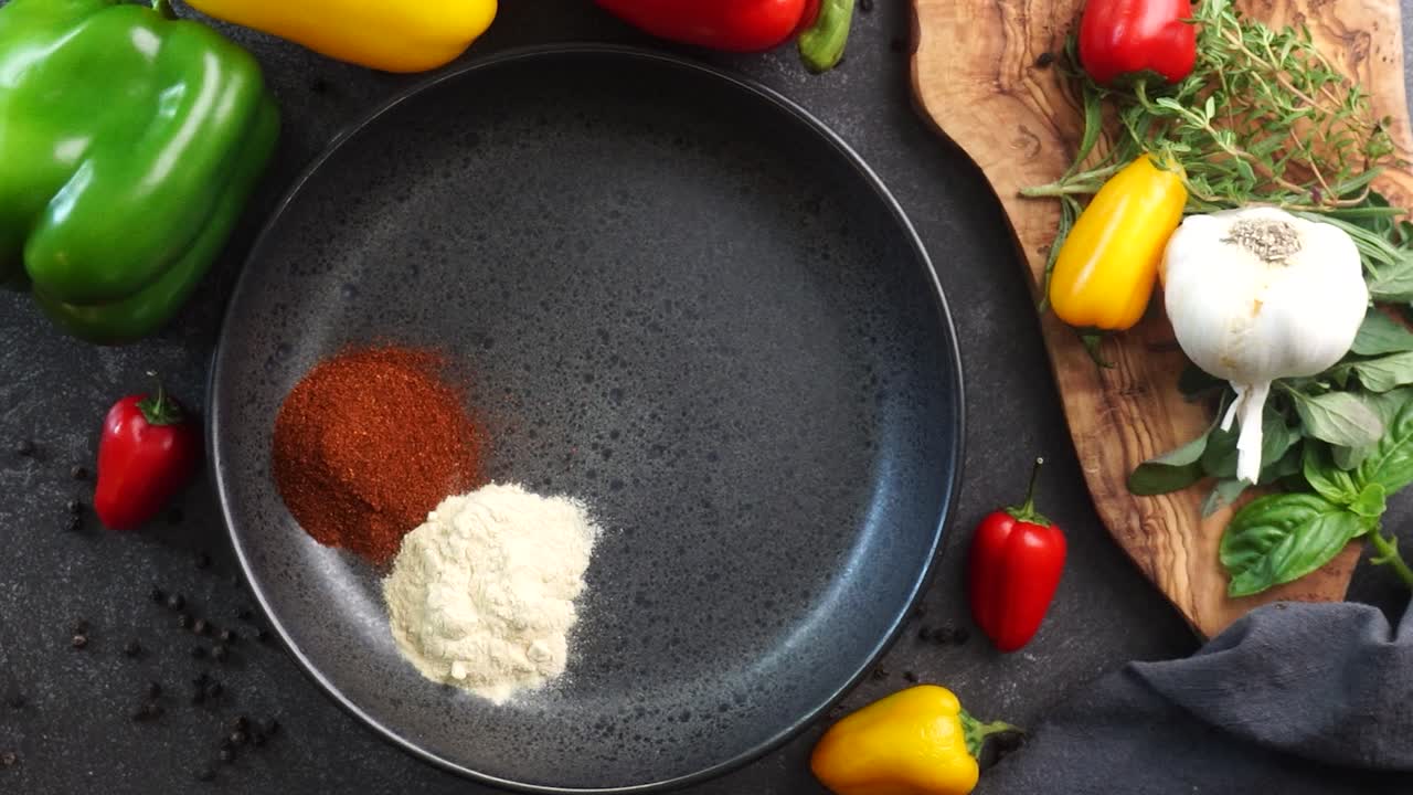 Making a vibrant Cajun Spice Blend, mixing red paprika, cayenne pepper, oregano, thyme, white garlic onion powder and black pepper in a bowl, creating a striking contrast against a black background.