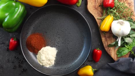 making a vibrant cajun spice blend, mixing red paprika, cayenne pepper, oregano, thyme, white garlic onion powder and black pepper in a bowl, creating a striking contrast against a black background.