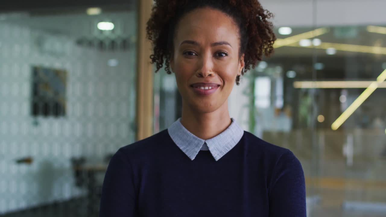 retrato de una mujer de negocios de raza mixta sonriente en un suéter azul de pie en la oficina