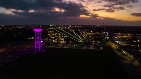 hyperlapse of modern office building with glowing water tower at night time, aerial