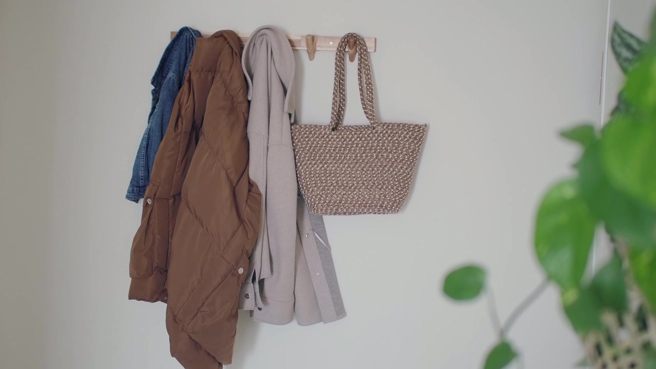 Cappotti e una borsa intrecciata appesi a un appendiabiti a muro in legno in una casa