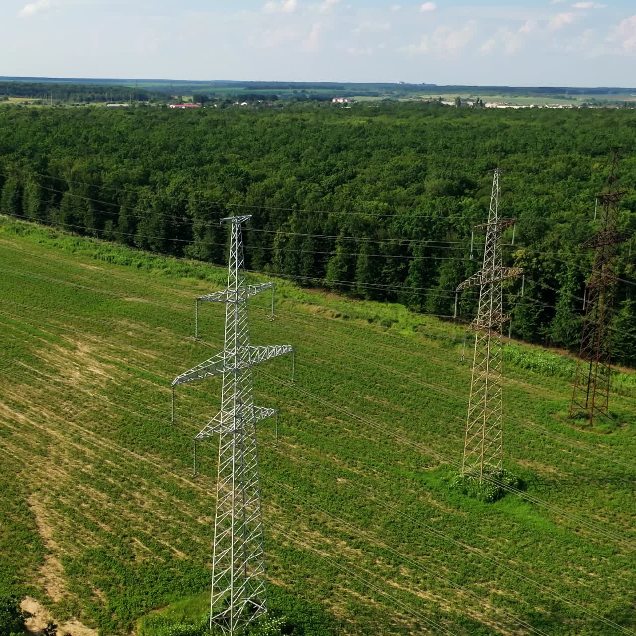 Transmission lines near green forest. High voltage electric line in the field. Steel pylons for electricity on beautiful nature background. Aerial view.