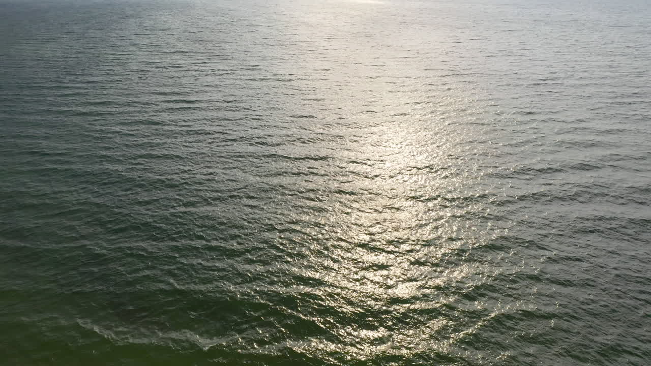 AERIAL: Locked Shot of Waves Crashing on the Surface of Reflective Sea