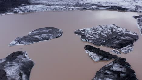 icebergs con ceniza negra flotando en una laguna glacial en el glaciar kvíarjökull, antena