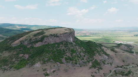 a super wide aerial drone shot makes a sweeping orbit around the majestic măgura uroiului mountain in romania, revealing the sheer rock cliff and the vast surrounding plain