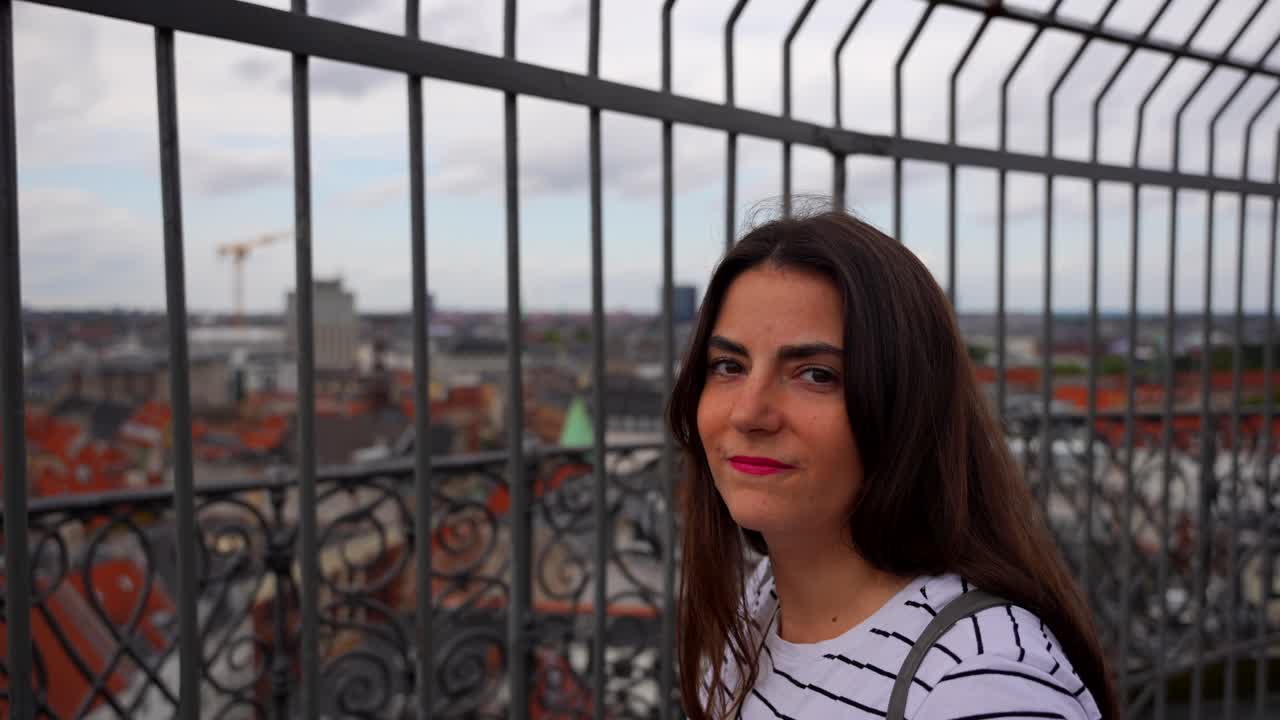 una mujer sonríe a la cámara mientras disfruta de la vista de copenhague desde la cima de rundetaarn