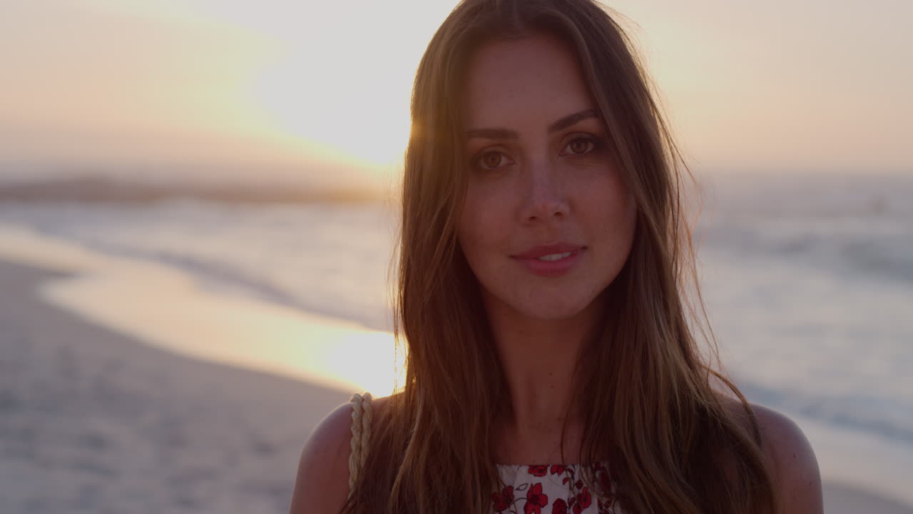 portrait of happy young woman turns head smiling enjoying summer vacation running hand through hair on beach sunset slow motion