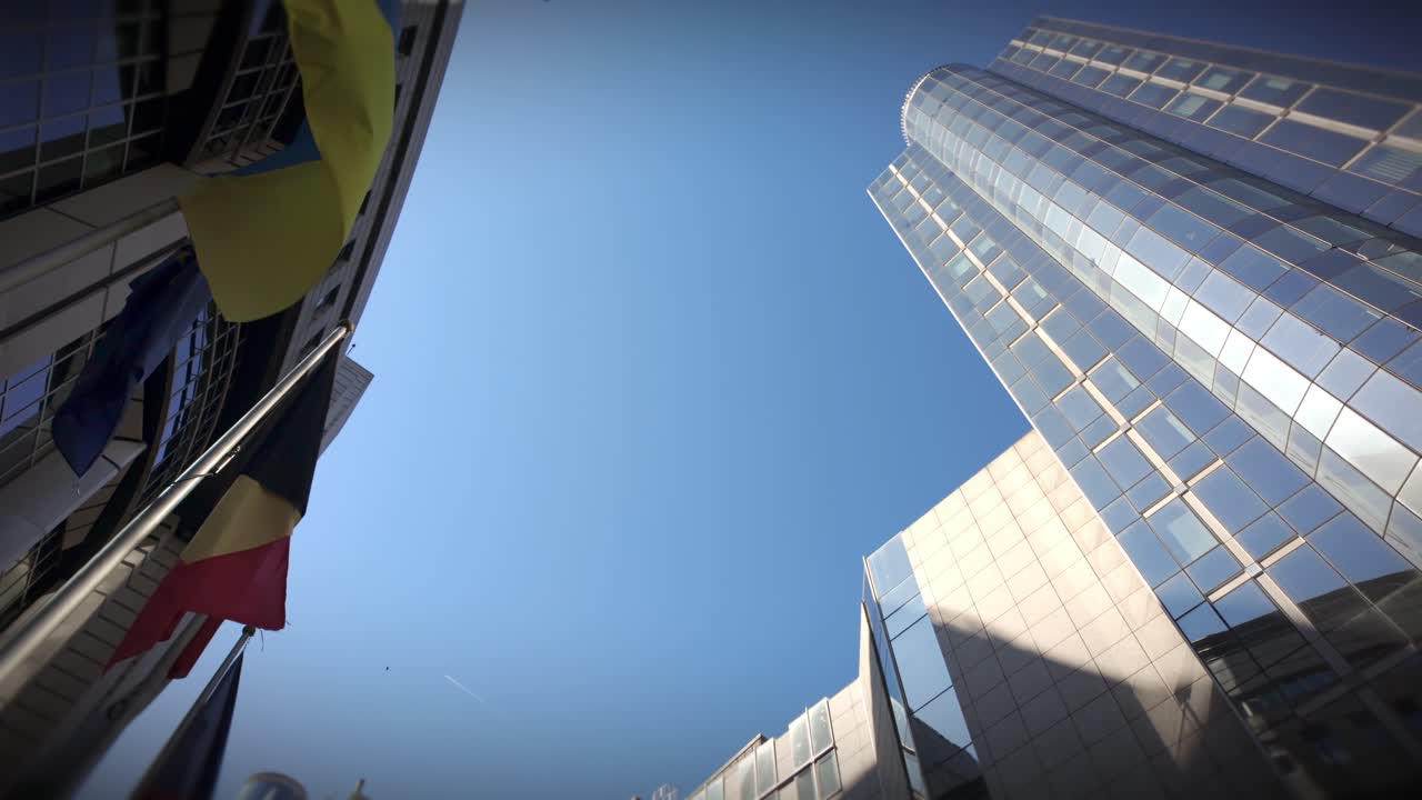 Low-angle shot of Ukraine, EU, Belgium flags and EU Parliament skyscraper