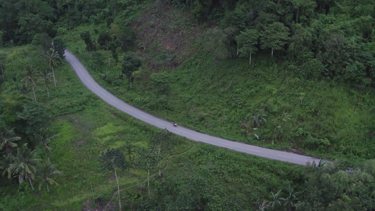 Sepeda motor melaju di jalan lokal kecil Indonesia yang dikelilingi pohon kelapa di pulau Sumba, dari udara.