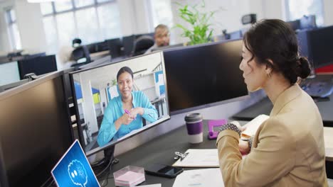 Asian-businesswoman-in-office-using-computer-with-video-call-and-ai-messaging-on-screens