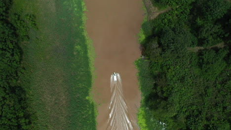 cinematic downward angle drone shot with a boat with wake on the amazon river and the rainforest surrounding the river in peru, following shot