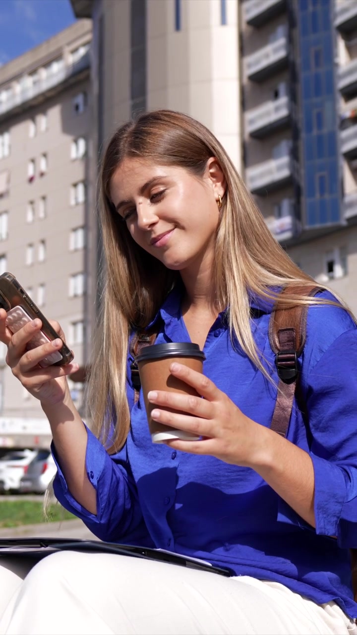 Giovane donna che usa lo smartphone e tiene in mano una tazza di caffè all'aperto