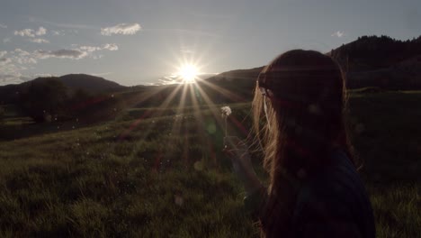 Woman-blowing-a-dandelion-seed-pod-during-sunset