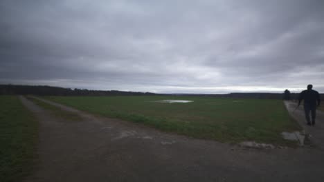 Modern-Black-Swordsman-Warrior-Awaiting-Battle-Opponent-in-Open-Field-Under-Grey-Sky,-Europe,-4K-|-Muscular,-Intimidating,-Shadow,-Figure,-Blurry,-Dark-Clothes,-Powerful,-Blurry,-Puddle,-Distance-Walk