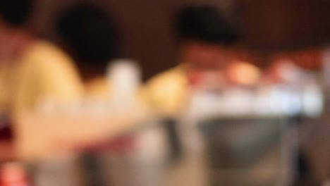 indistinct figures in yellow attire working behind a kitchen counter with various containers.