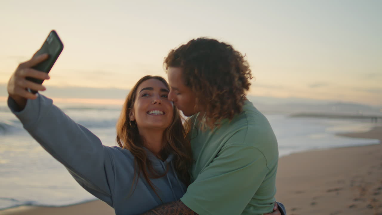 una pareja tomando una selfie en la playa al atardecer.