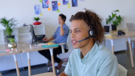 young mixed-race male executive talking on headset at desk 4k