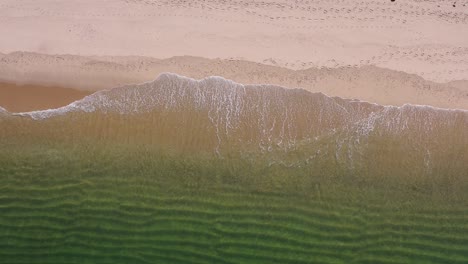 a-birds-eye-view-of-small-waves-breaking-on-the-golden-sand