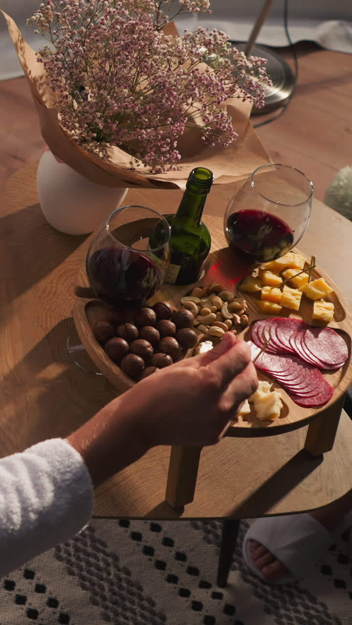 Breaded man eats cheese on skewer near glamping house. Handsome guy in terry bathrobe enjoys delicious appetizer for gourmets with wine. Relaxation evening