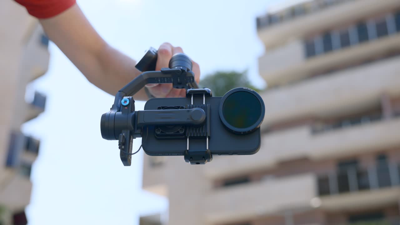 Close-up of hand operating FeiyuTech Scorp Mini gimbal with smartphone. Vlogger or content creator filming outdoors. For technology or social media content