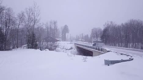 Luftaufnahme-In-Zeitlupe-Eines-Lastwagens,-Der-Während-Eines-Schneesturms-Einen-Schneemobilanhänger-über-Eine-Brücke-Schleppt