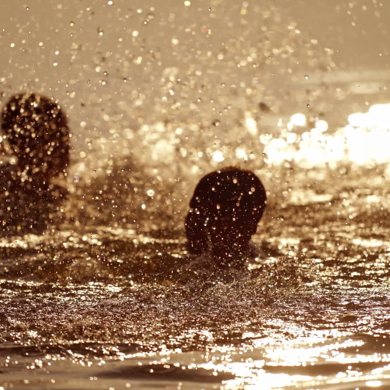 Two boys splashing with water happily at sunset. Silhouette of kids heads playing in the river water during summer holidays in the evening. Joyful summertime.