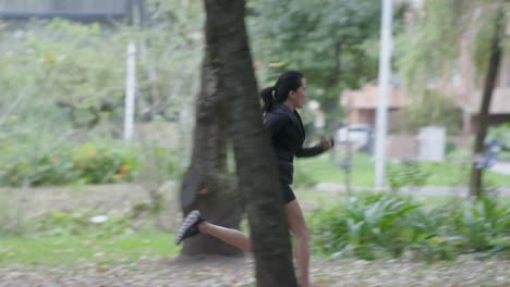 a woman in an all-black costume does her morning jog on the edge of the city park