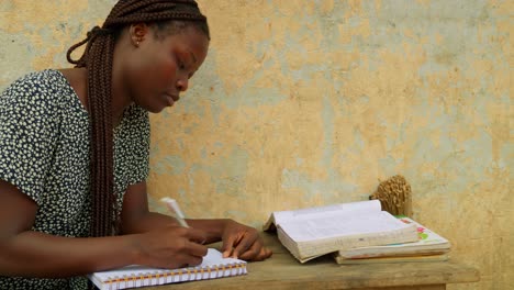 Una-Colegiala-Local-Copiando-Notas-De-Un-Libro-Mientras-Estudiaba-En-Una-De-Las-Aldeas-De-Kumasi,-Ghana,-África