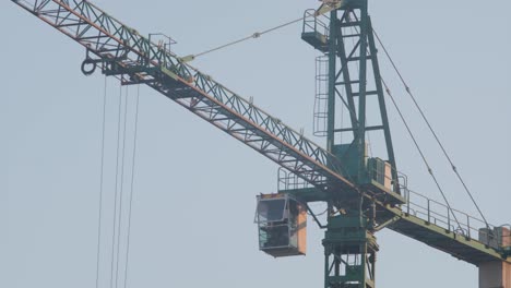 side view of a stationary tower crane, featuring the operator's cabin, with a clear blue sky in the background.