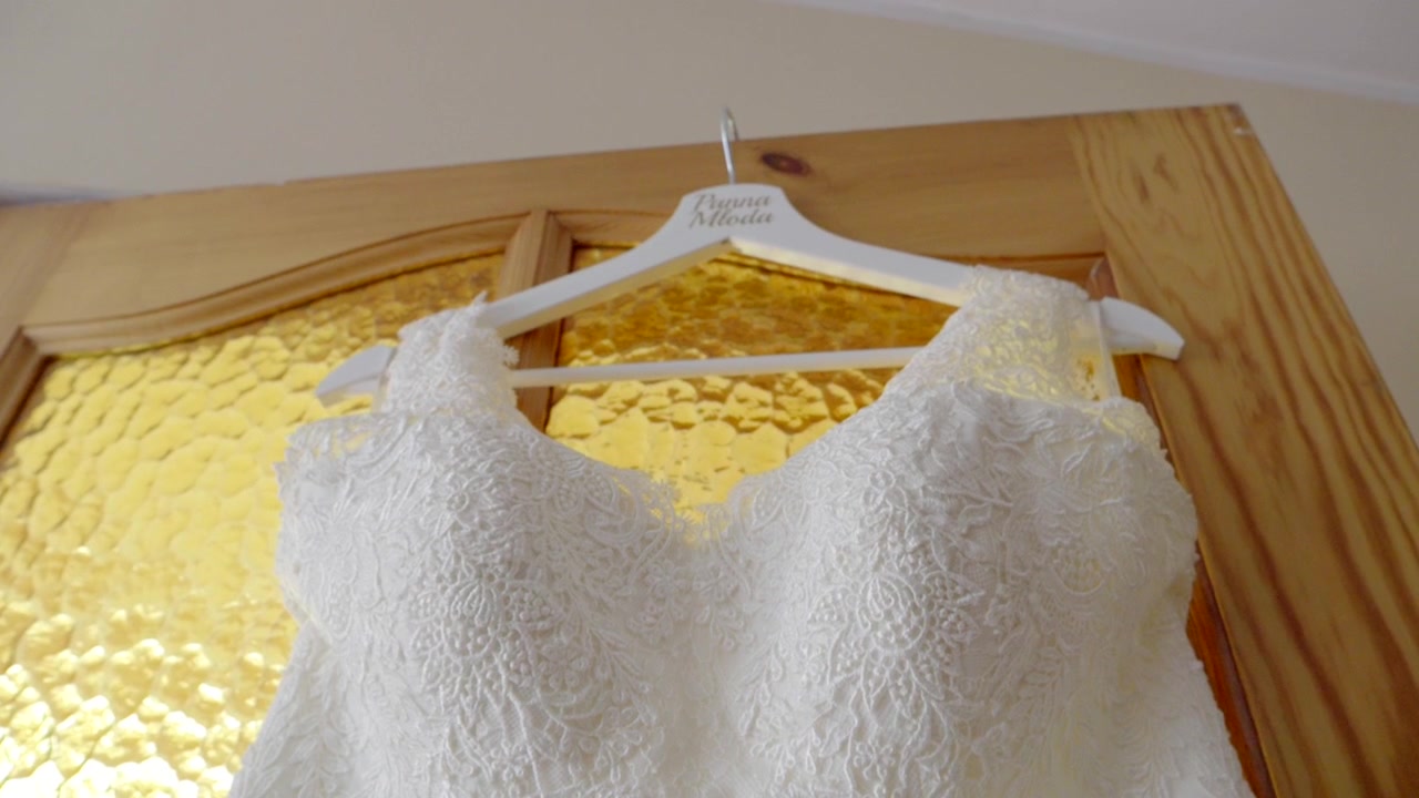Un vestido de novia blanco colgado en puertas de madera, esperando los preparativos de la novia