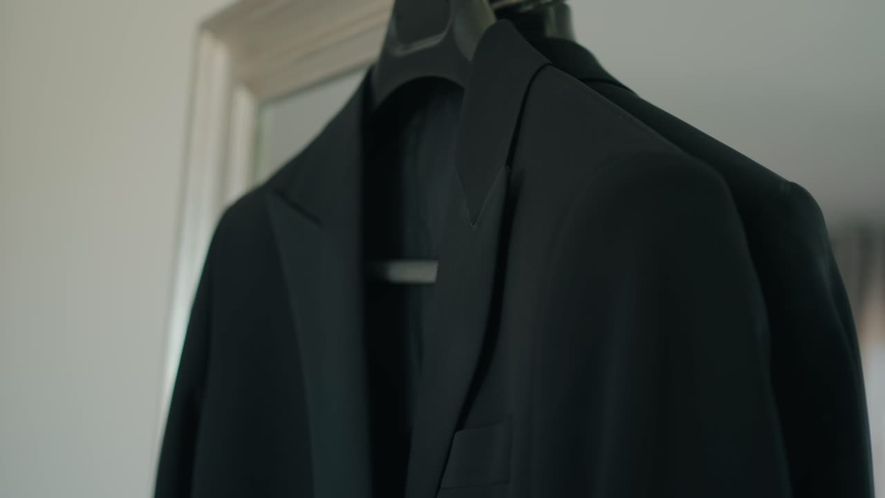 밝은 창문 옆 옷걸이에 걸려 있는 검은색 양복