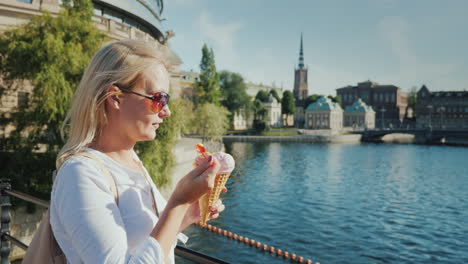 Mujer-Turista-Comiendo-Helado-En-El-Fondo-De-La-Vista-Reconocible-De-La-Ciudad-De-Estocolmo-I