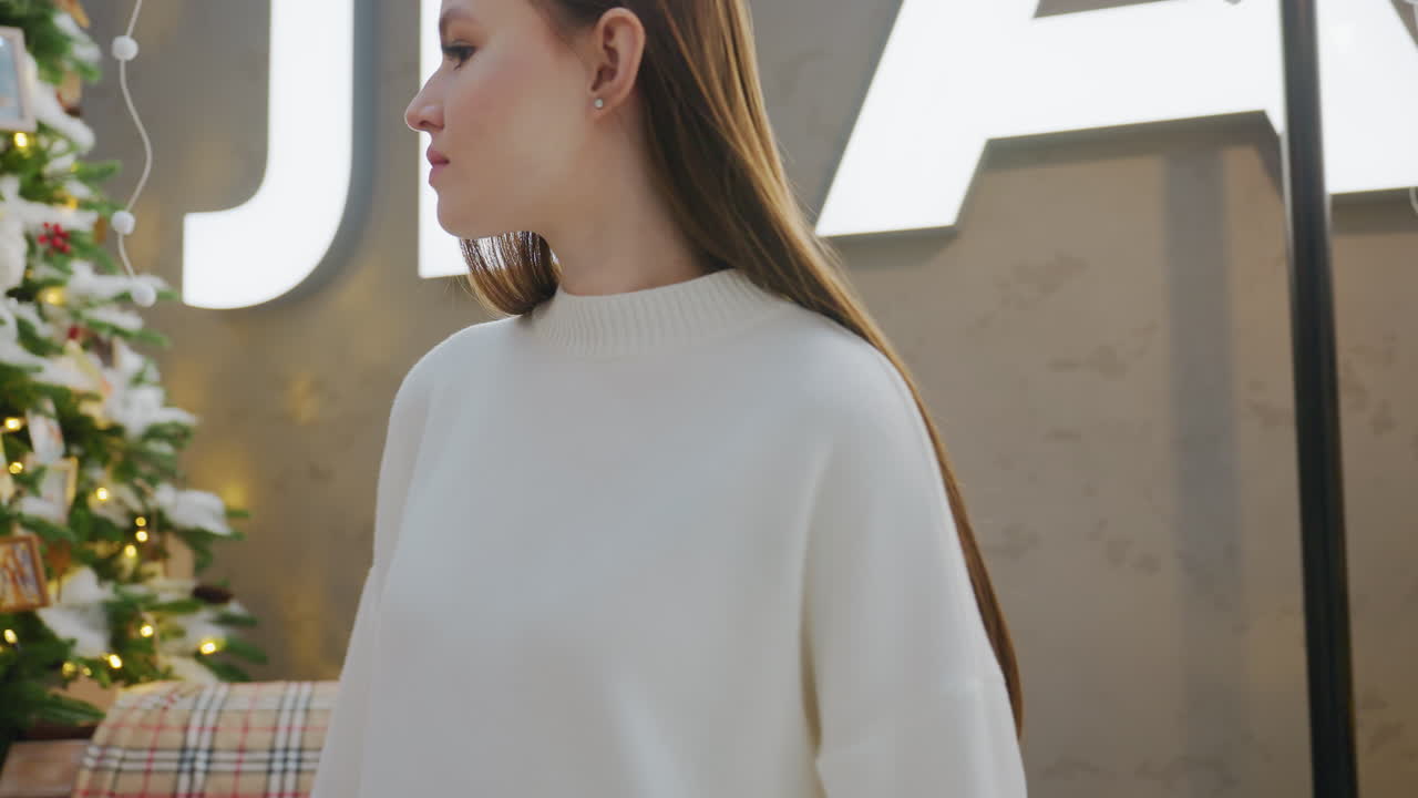 Close-up of lady walking past decorative seat with inscription on the wall and festive plants, walking towards seat amidst Christmas decorations and twinkling lights
