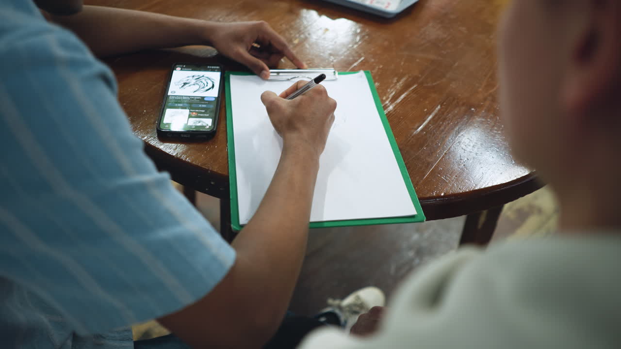 Overhead shot showing shiny wooden table surface with smartphone and blank paper sheet side by side capturing minimalist workspace aesthetic with warm natural light reflecting off polished grain
