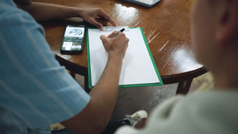 overhead shot showing shiny wooden table surface with smartphone and blank paper sheet side by side capturing minimalist workspace aesthetic with warm natural light reflecting off polished grain