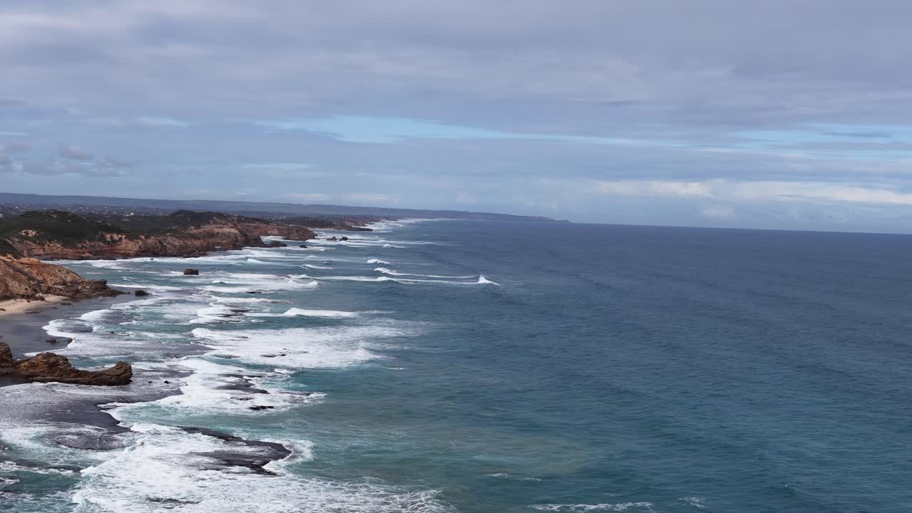 Drone pans over rugged Sorrento coastline, capturing waves, rocky shore, and overcast natural lighting