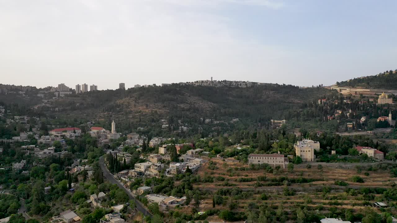vuelo aéreo sobre un pueblo árabe en la zona de jerusalén, edificios en la ladera de una colina con vegetación forestal verde