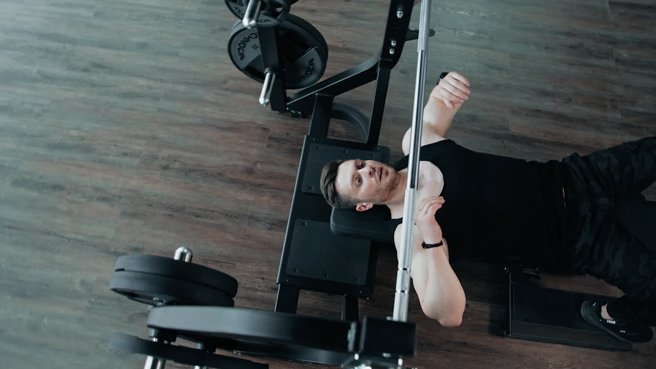 Adam spor salonunda ağırlık kaldırıyor. Profesyonel sporcunun bench press yaparken üstten görünümü.