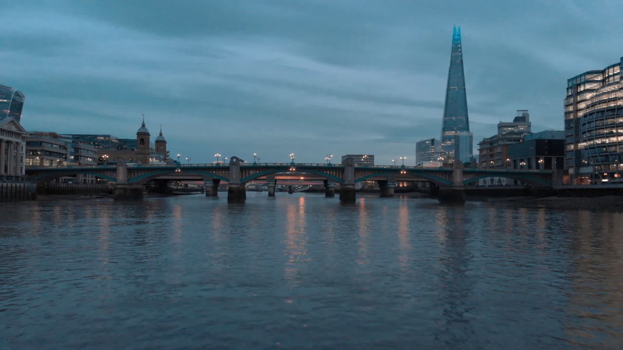 disparo de un dron bajo a lo largo del río támesis bajo el fragmento del puente de southwark en el fondo a la hora azul del atardecer